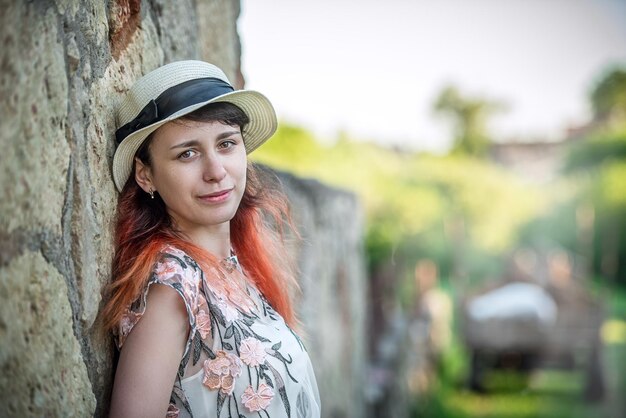 Fille aux cheveux rouges dans un chapeau appuyé contre un mur rétro en pierre