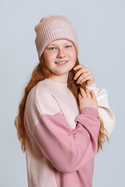 Une fille aux cheveux rouges dans un pull et un chapeau redresse ses cheveux un