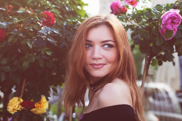 Fille aux cheveux rouges dans une robe noire. Buissons de roses.