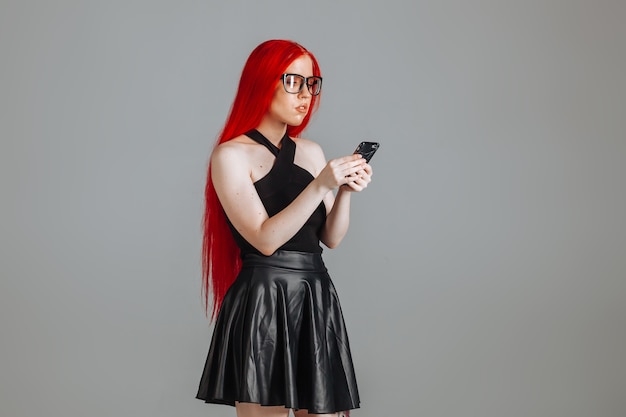 Fille aux cheveux rouges portant des lunettes et un message de types jupe en cuir au téléphone