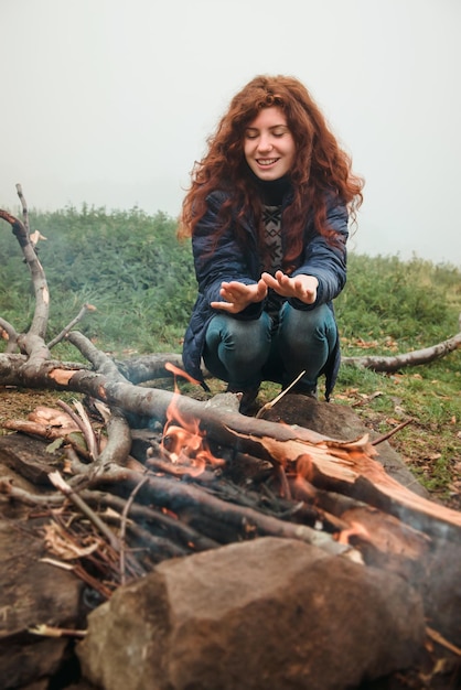 Fille aux cheveux rouges se réchauffant les mains près du feu de camp