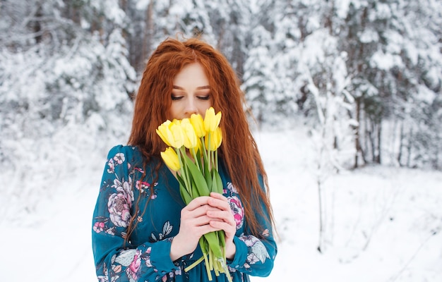 Une fille aux cheveux rouges tient un bouquet de tulipes jaunes sur un paysage d'hiver