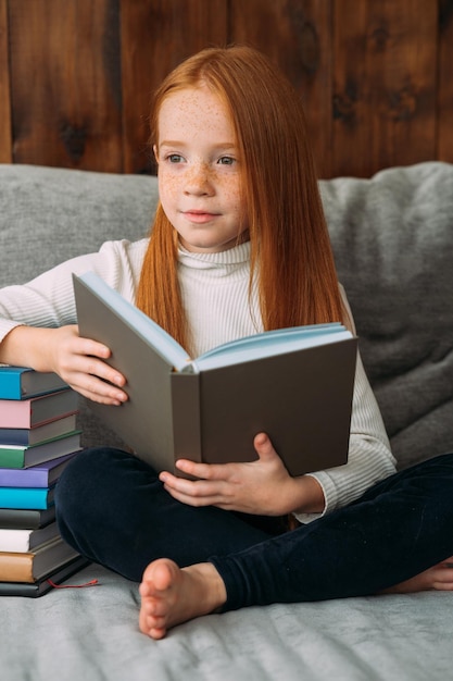 Une fille aux cheveux roux avec un livre dans les mains est assise dans la position du lotus et lit