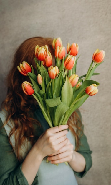 Photo la fille aux cheveux roux se couvre le visage de tulipes rouges et jaunes