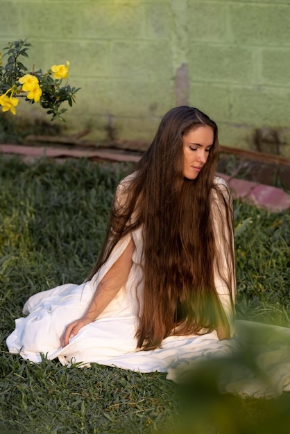 Une fille aux cheveux très longs est assise sur l'herbe dans un paysage torpique. Robe blanche de la mariée. Santé