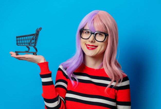 Fille aux cheveux violets et pull rouge tenir un caddie noir sur fond bleu