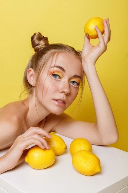 Fille aux citrons sur un mur jaune avec un maquillage lumineux. humeur estivale