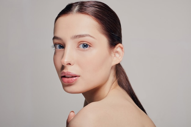 Fille aux lèvres charnues, aux cheveux noirs et à la peau radieuse, propre et délicate, elle pose sa main sur l’épaule, droite, grise. Soulever, femme bien soignée. Spa.