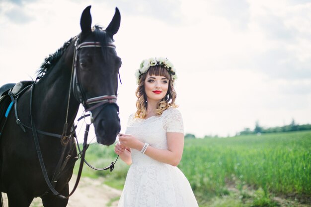 Fille aux lèvres rouges dans une robe blanche près d'un cheval noir