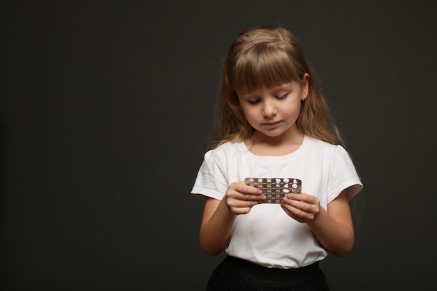 Une fille aux longs cheveux blonds tient des pilules dans ses mains et les regarde.