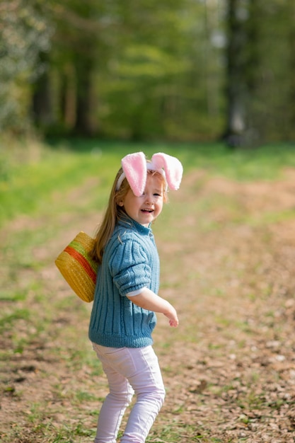 Une fille aux oreilles de lapin recueille des œufs en chocolat dans un panier pour Pâques