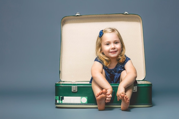 Fille aux pieds nus assis à l'intérieur d'une vieille valise.