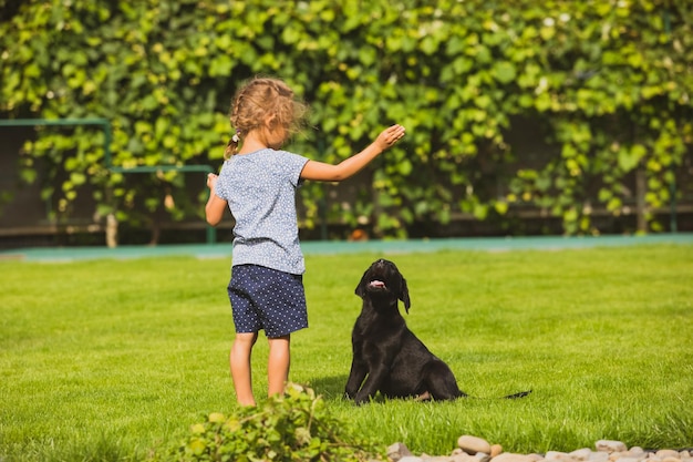 Une fille aux pieds nus joue avec un adorable chiot labrador noir