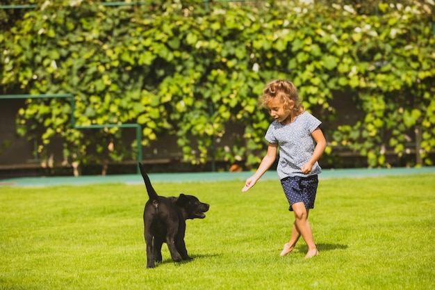 Une fille aux pieds nus joue avec un adorable chiot labrador noir