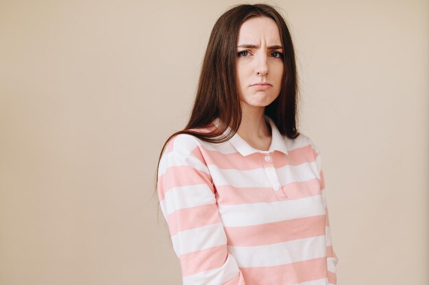 La fille aux sourcils froncés serre les sourcils et les lèvres Belle jeune femme vêtue d'un cardigan rayé se tient sur fond