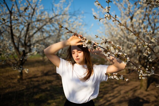 fille aux yeux fermés posant près des arbres en fleurs au printemps.