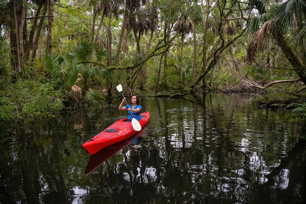 Fille aventureuse faisant du kayak sur une rivière couverte d'arbres