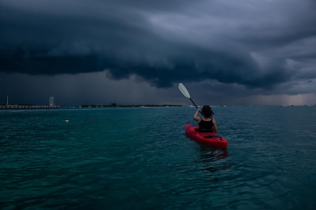 Une fille aventureuse sur un kayak rouge fait du kayak vers un orage pendant un coucher de soleil spectaculaire