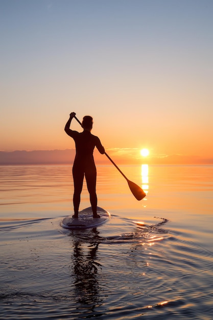 Une fille aventureuse sur une planche à pagaie pagaie pendant un coucher de soleil lumineux et vibrant