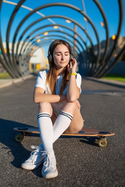 fille en bas blancs s'asseoir sur le longboard et écouter de la musique