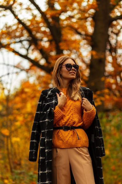 Fille de beauté caucasienne à la mode avec des lunettes élégantes dans des vêtements de mode d'automne avec manteau et pull à l'extérieur