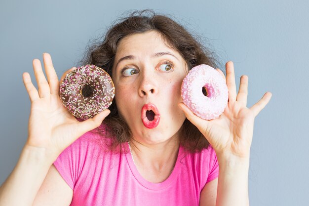 Fille de beauté prenant des beignets colorés. Femme joyeuse drôle avec des bonbons, dessert. Régime alimentaire, concept de régime. Malbouffe, Célébration et fête.