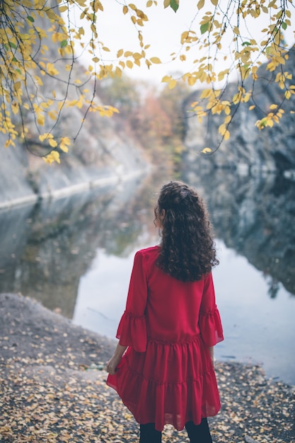 Fille de beaux cheveux bouclés dans une robe rouge en regardant le lac