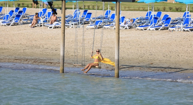 fille en bikini se balançant sur une balançoire sur le rivage
