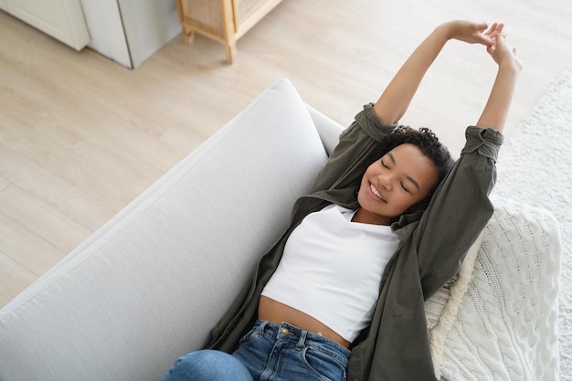 Une fille biraciale souriante se repose sur un canapé à la maison qui s'étend du corps se réveillant après le sommeil