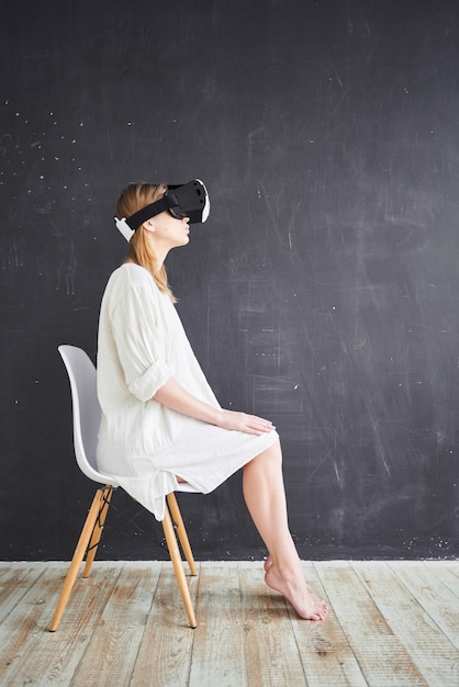 La fille en blanc assise sur une chaise dans le casque de réalité virtuelle