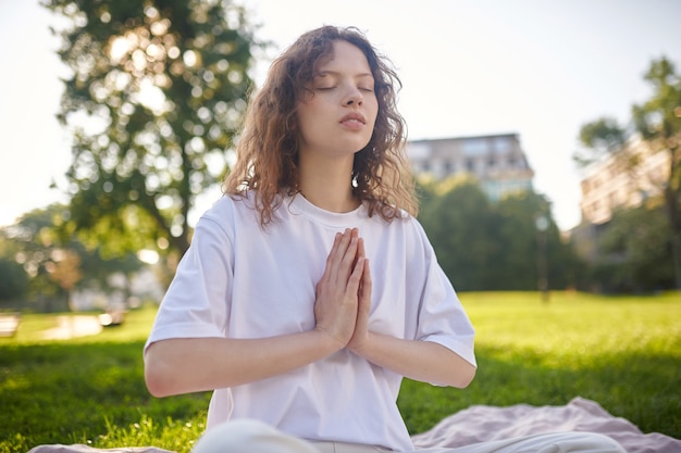 Une fille en blanc méditant dans le parc et ayant l'air paisible