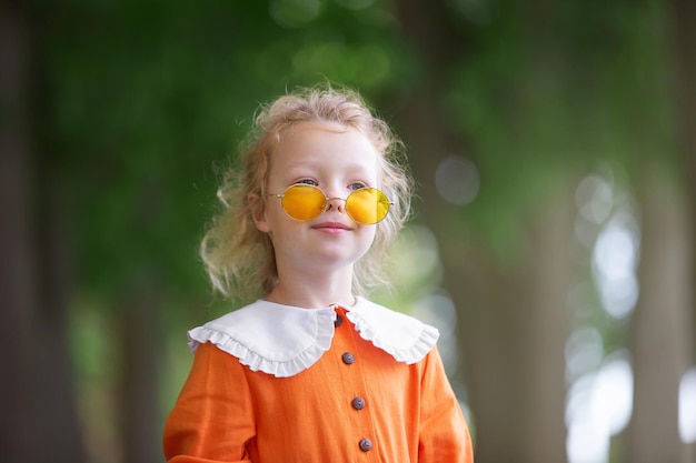 une fille blonde d'âge préscolaire dans une couronne de rowan et avec des jouets se promène dans le parc un matin d'été