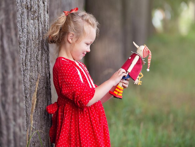 une fille blonde d'âge préscolaire dans une couronne de rowan et avec des jouets se promène dans le parc un matin d'été