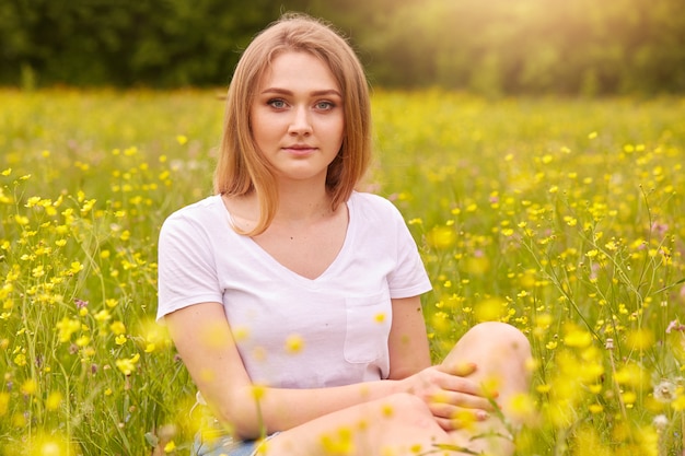 Fille blonde assise entourée de fleurs de champ jaune