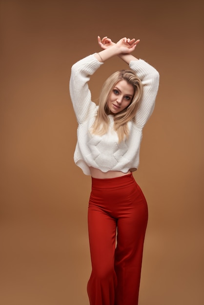 Fille blonde chaude en pantalon rouge posant en marron