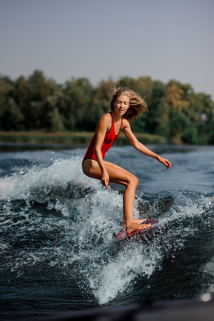 Fille blonde à cheval sur le wakeboard rouge sur le lac