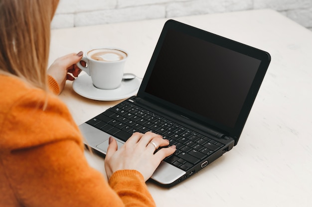 Fille Blonde Dans Un Café Avec Un Ordinateur Portable Et Un Café. Pigiste Jeune Fille Travaillant Sur Un Ordinateur Portable