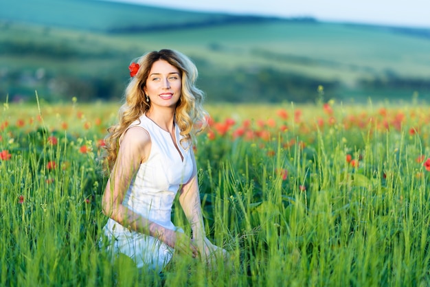 Fille blonde dans le champ de coquelicots, souriant dans le pré de la nature