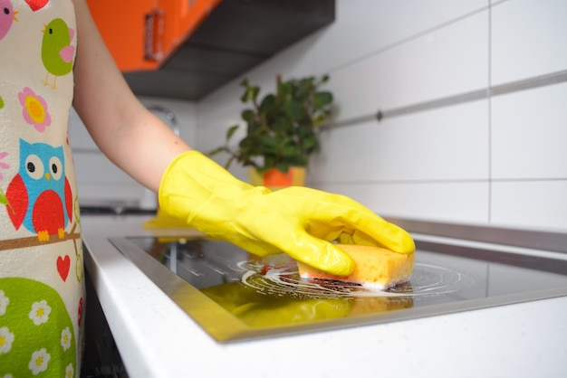 Fille blonde dans les gants jaunes avec une éponge essuyant la cuisinière à induction électrique en céramique haut de gamme grand angle Espace de copie