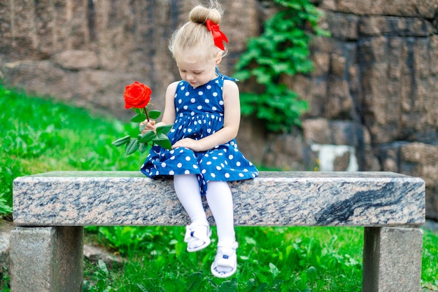 Fille blonde dans le parc est assise sur un banc avec une rose