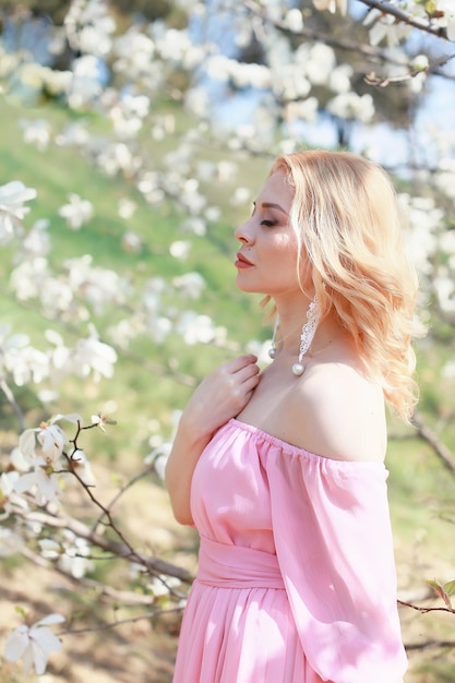 Une fille blonde dans une robe rose près d'un magnolia.