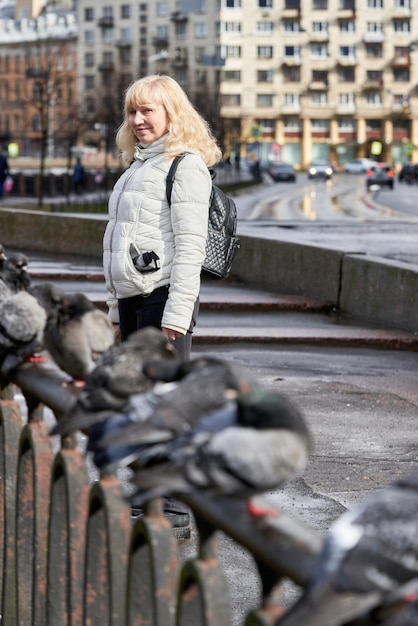 Fille blonde dans une veste légère à côté d'une clôture métallique et de pigeons assis dessus