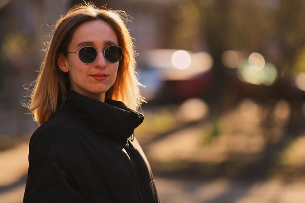 Une fille blonde dans une veste noire et des lunettes de soleil noires marche dans la rue