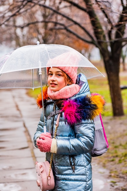 Fille blonde dans une veste avec un parapluie transparent sous la pluie à l'extérieur dans le froid