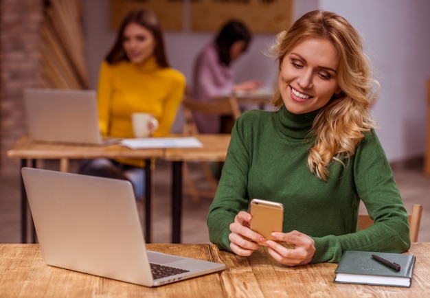 Fille blonde dans des vêtements décontractés à l'aide de smartphone et ordinateur portable.