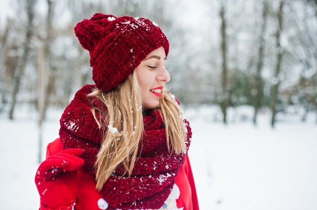 Fille blonde en écharpe rouge, bonnet et pull de père Noël posant au parc le jour de l'hiver.