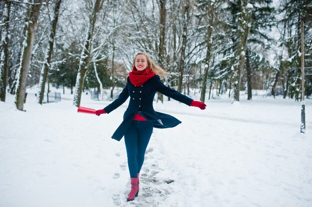 Fille blonde en écharpe rouge et manteau marchant au parc le jour d'hiver.