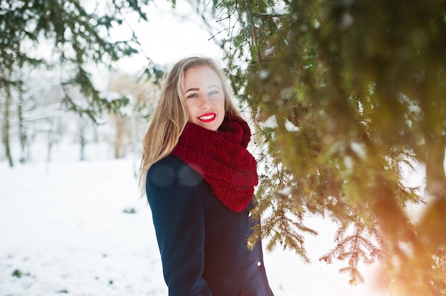 Fille blonde en écharpe rouge et manteau marchant au parc le jour d'hiver.