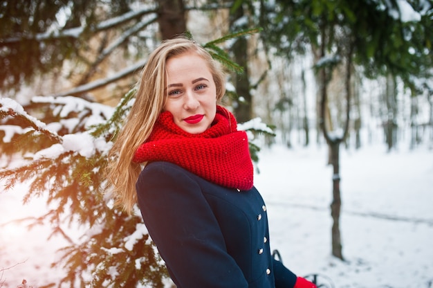 Fille blonde en écharpe rouge et manteau à pied au parc le jour de l'hiver.