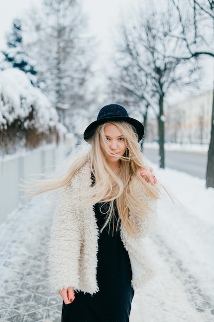 Fille blonde élégante aux longs cheveux volants posant dans la rue